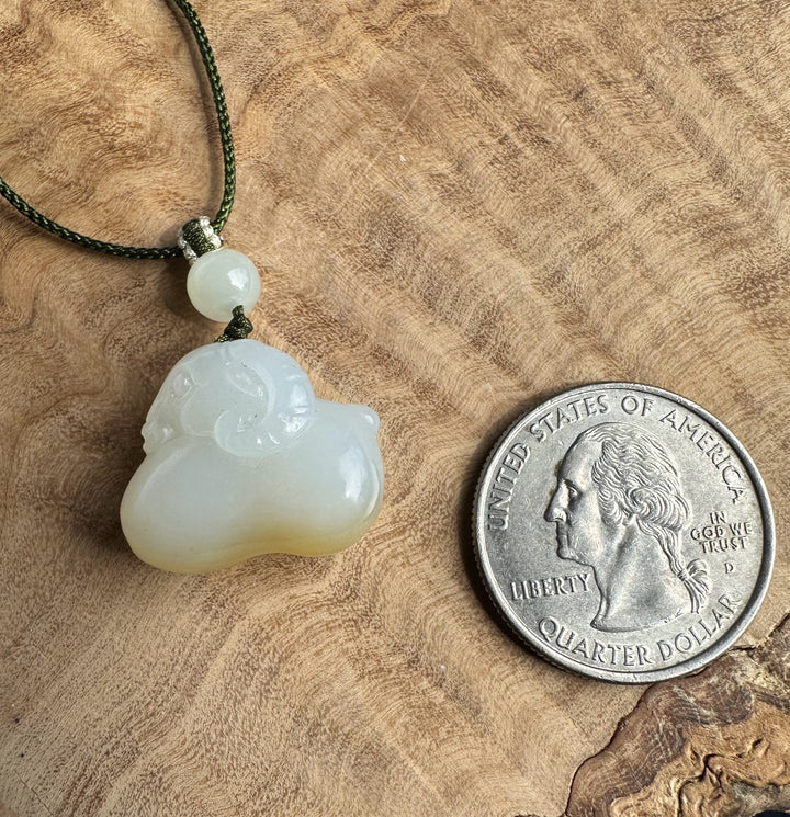 White and brown jade pendant on a wood surface beside a quarter for scale