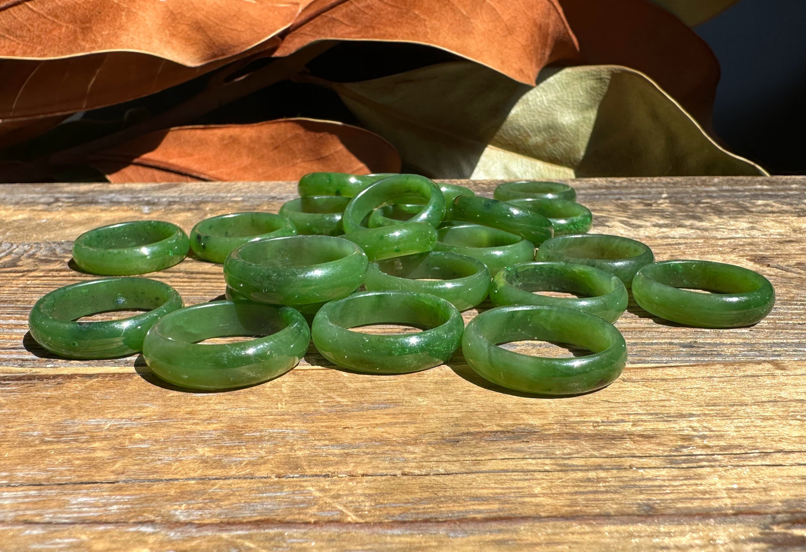 Group of jade band rings 6mm wide scattered on a weathered wooden surface.