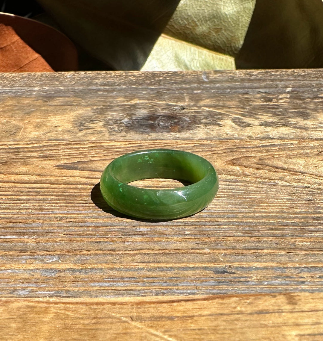 Close up of a jade band ring lying on wood with a leaf backdrop.