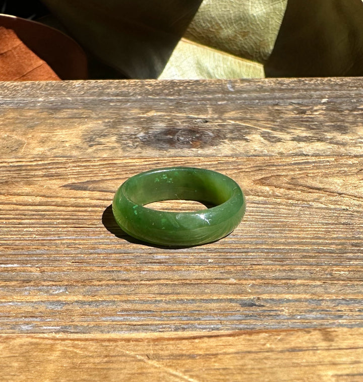 Close up of a jade band ring lying on wood with a leaf backdrop.
