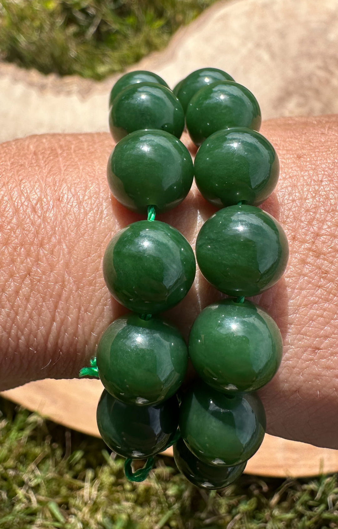 Round dark green beads on wrist with a grass background