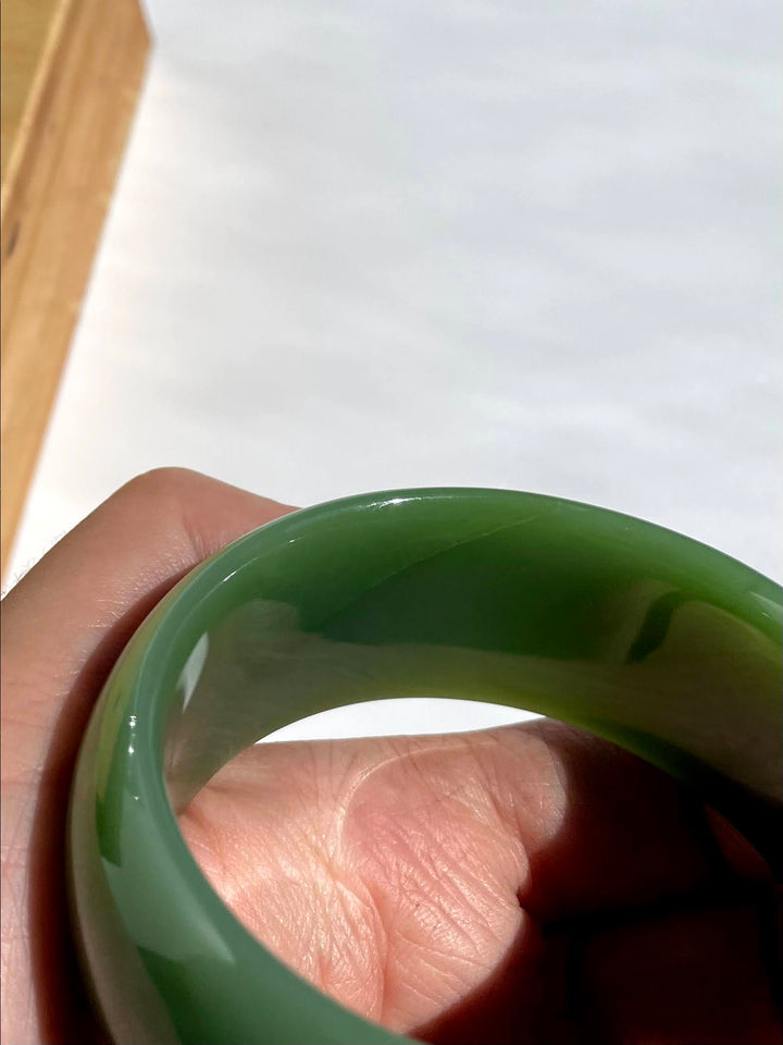 Close-up of a glossy green jade bangle being held by fingers