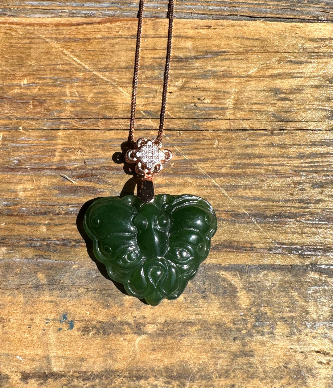 Dark green nephrite jade butterfly pendant on copper chain with a decorative floral bail against weathered wood