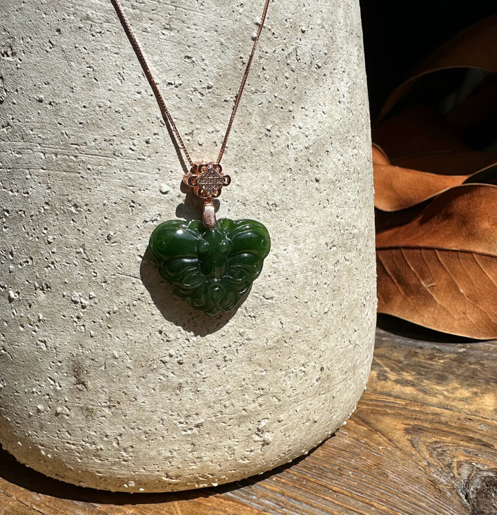 Dark green nephrite jade butterfly pendant on copper chain with a decorative flower bail against a textured stone surface.