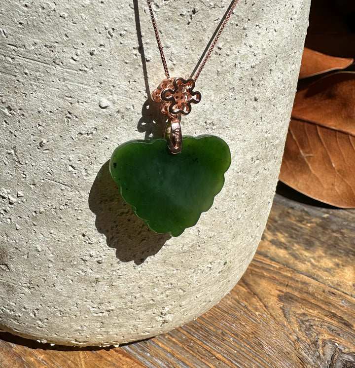 Brightly lit dark green nephrite jade butterfly pendant on copper chain against a sunlit textured background with wood.