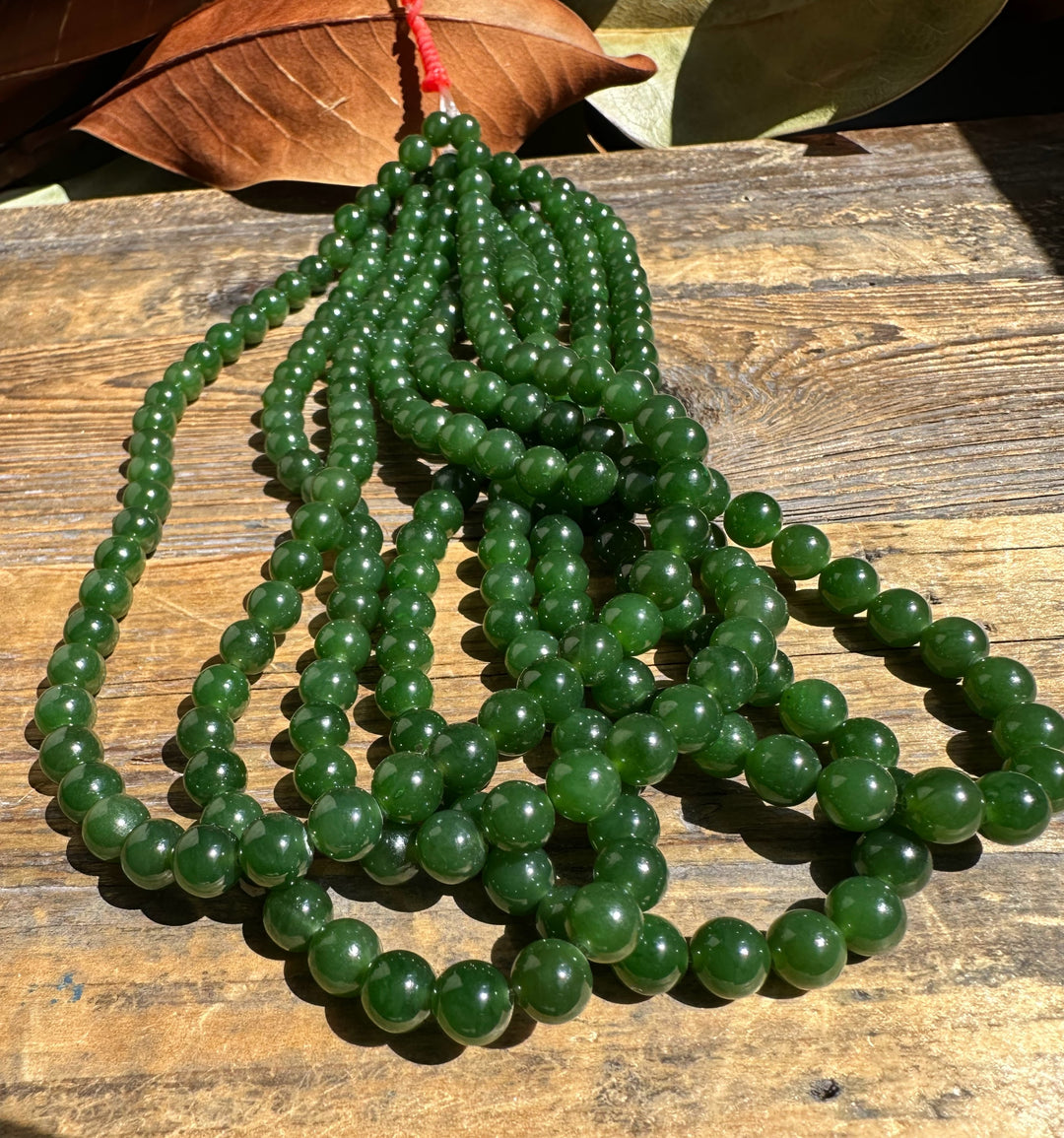 Unstrung seven millimeter nephrite jade beads in several strands on a wooden surface.