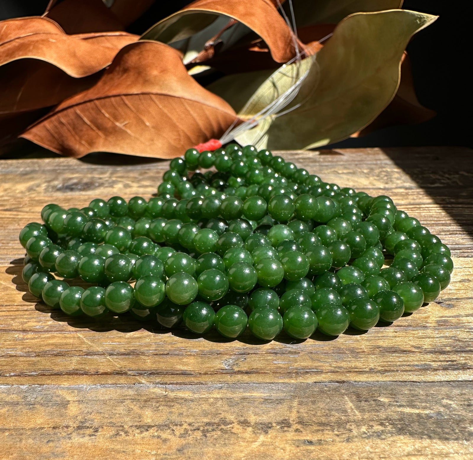 A 16 inch strand of 7mm nephrite jade beads unstrung on a wooden surface