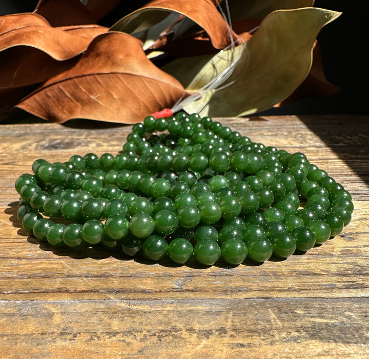 A 16 inch strand of 7mm nephrite jade beads unstrung on a wooden surface