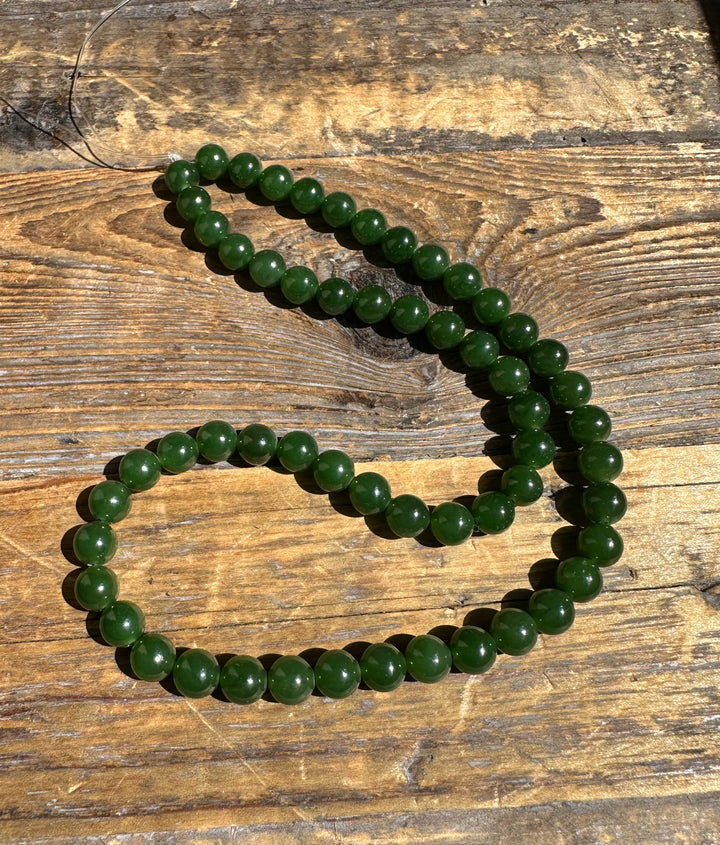 Unstrung seven millimeter nephrite jade beads laid out on a wooden surface.