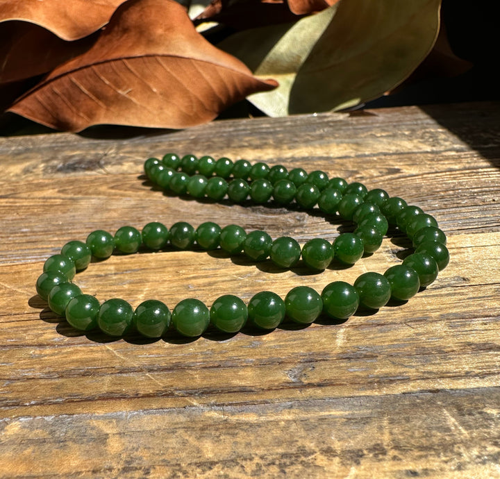 Nephrite jade beads 7mm unstrung 16 inches arranged in loops on a wooden surface