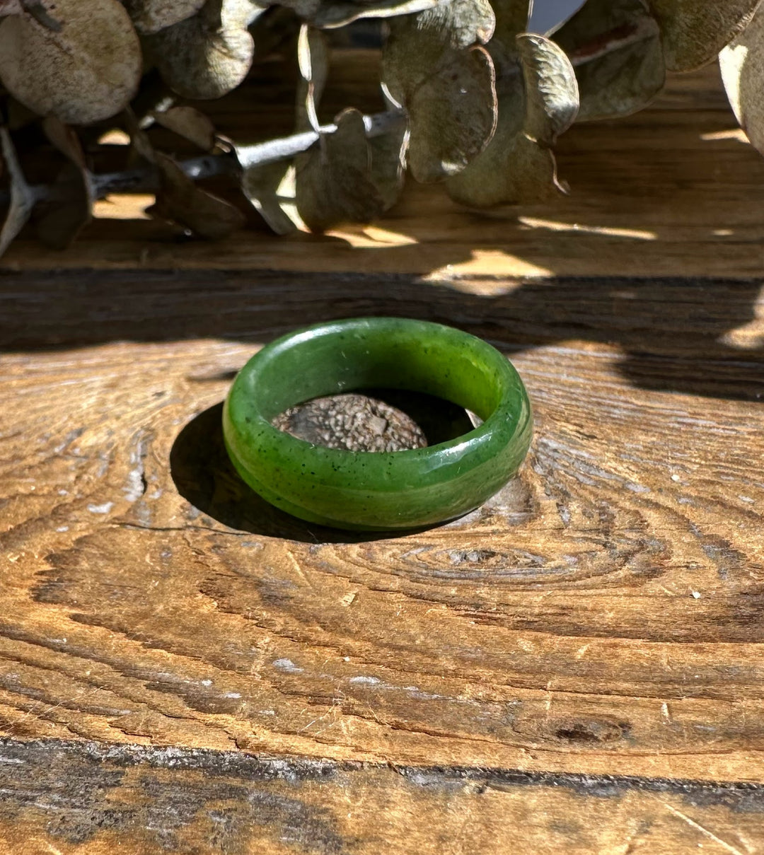 Single green jade band ring with a polished finish resting on sunlit wooden surface