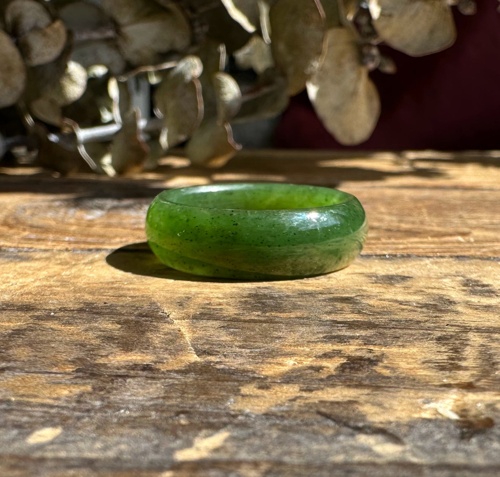 Jade band ring 6.5mm in bright green with a smooth polished surface on a rustic wooden table