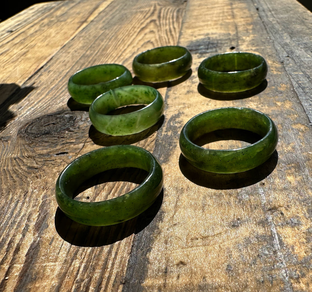 Six green jade band rings arranged on a weathered wooden surface.