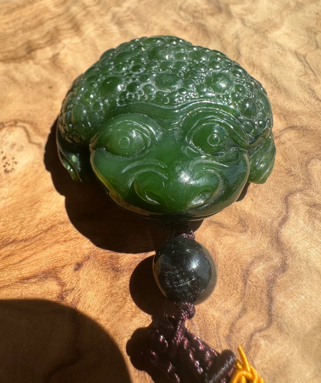 A carved green jade-like decorative object with a stylized face and textured top, shown on a wood surface with a dark bead and cord below.
