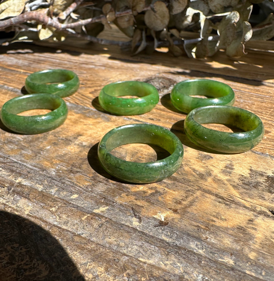 Five jade band rings in varying green tones arranged on a weathered wooden surface