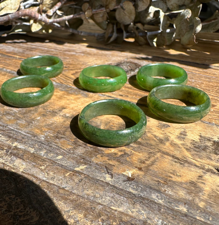 Five jade band rings in varying green tones arranged on a weathered wooden surface
