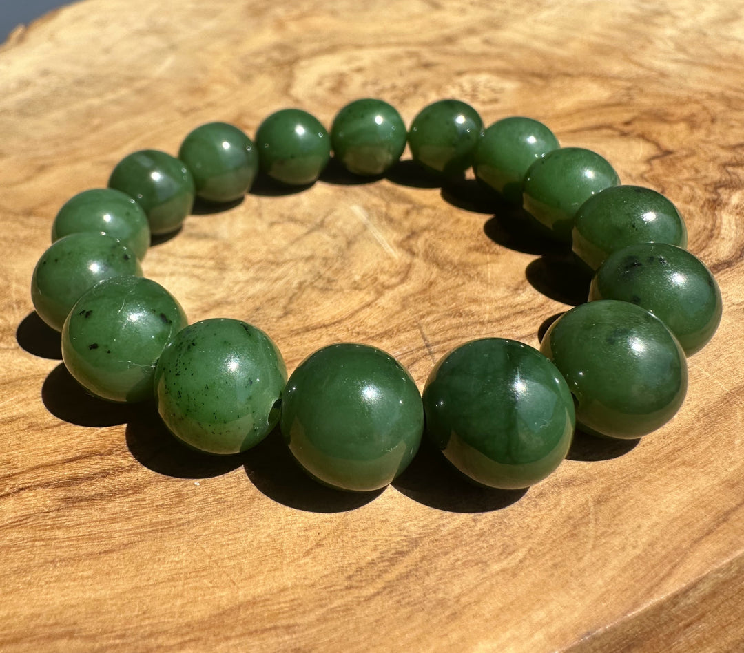 A beaded stretch bracelet made of polished dark green jade-like round beads, displayed on a textured wooden surface.