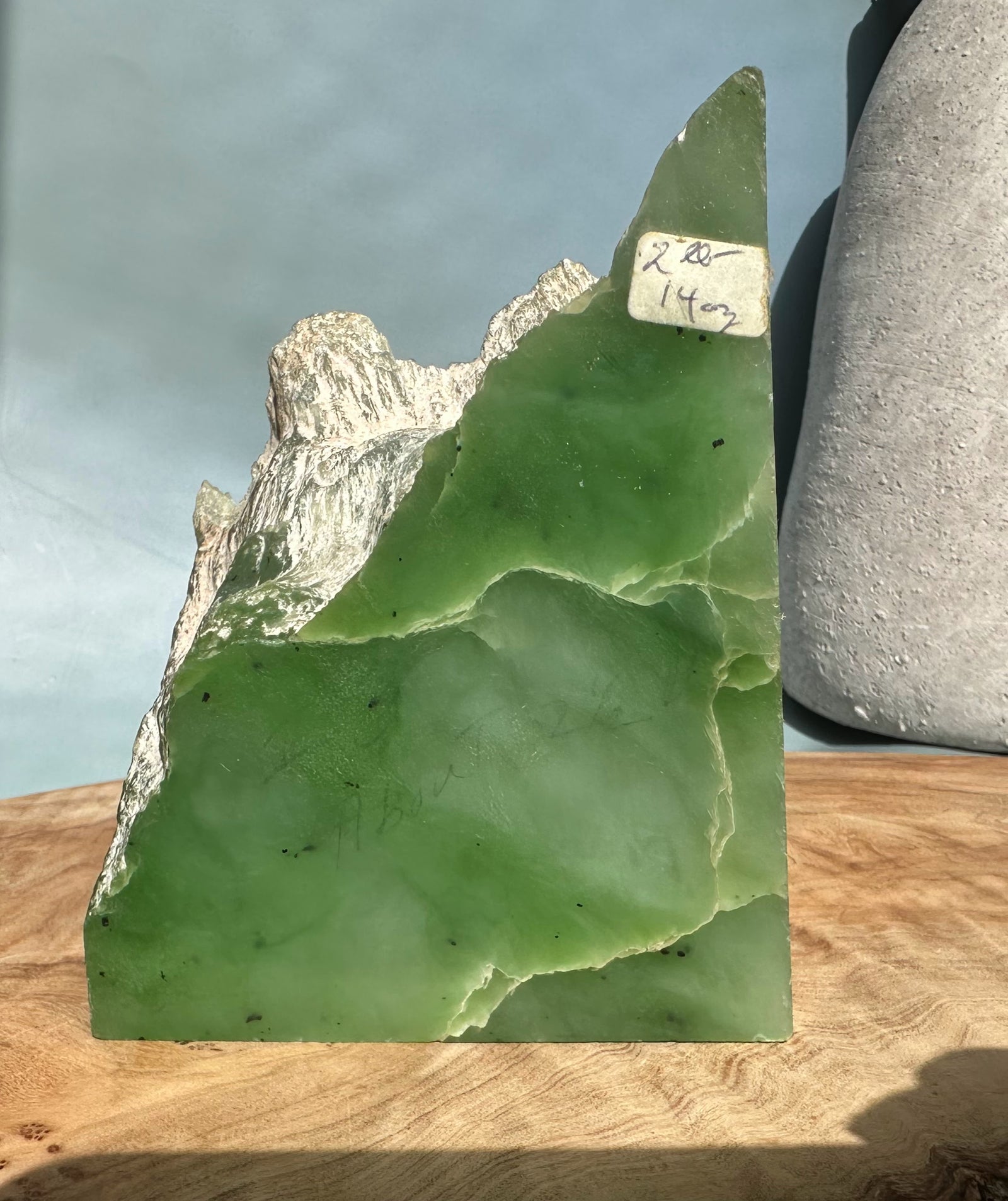 Light green nephrite jade chunk with white rock matrix edge and a handwritten label reading 2 lbs 14 oz.