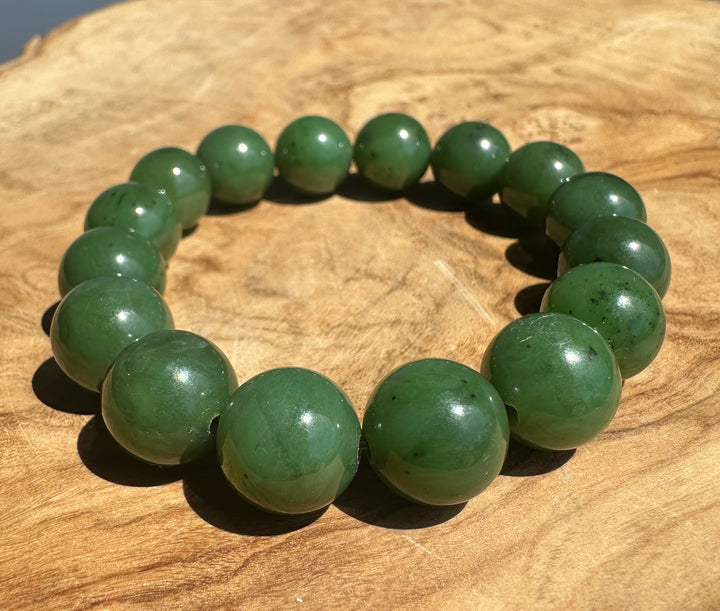 A beaded stretch bracelet made of polished green jade-like round beads, displayed on a natural wood slice background.