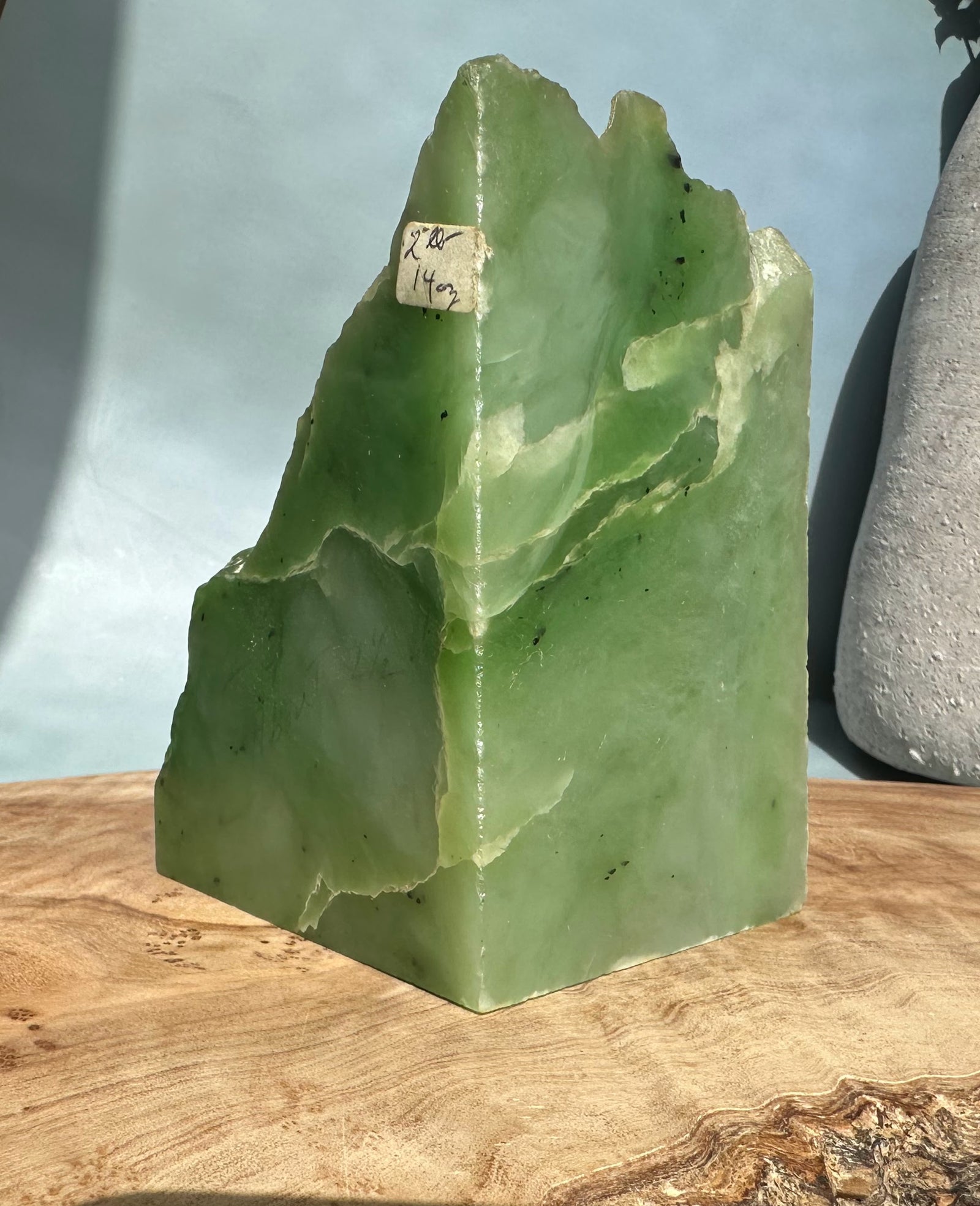 Tall light green nephrite jade block with a jagged peak and a small handwritten label on its front