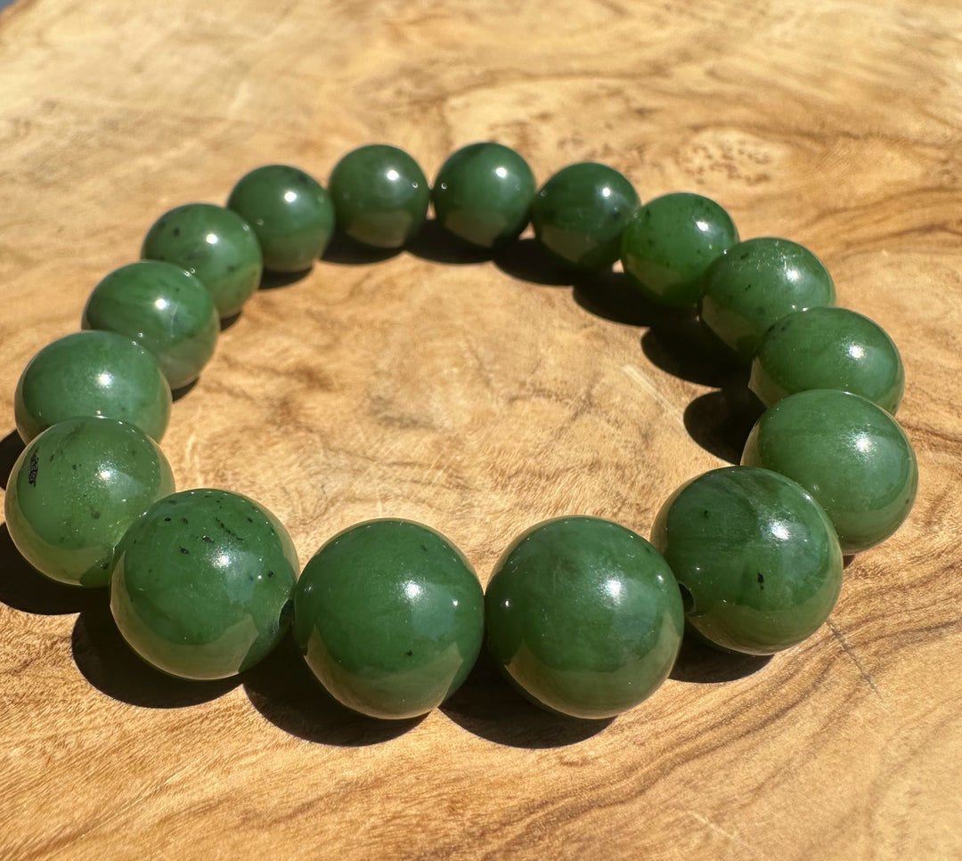A beaded bracelet made of polished green jade-like round beads, arranged in a circle on a textured wooden surface.