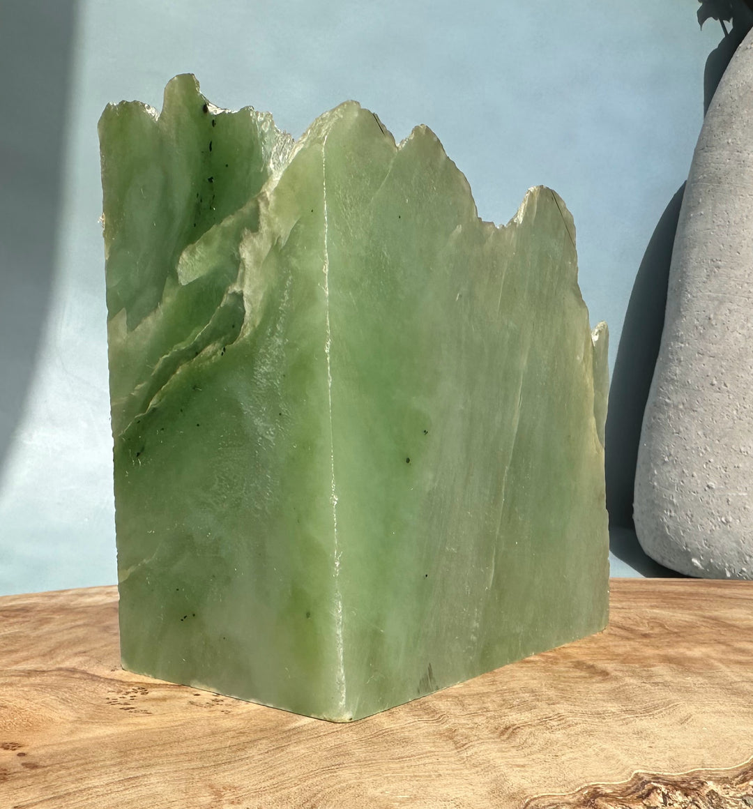 Siberian light green nephrite jade block with jagged top on a wooden surface