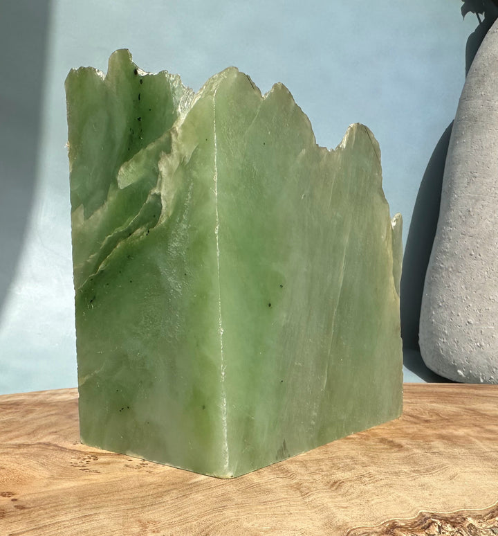 Siberian light green nephrite jade block with jagged top on a wooden surface