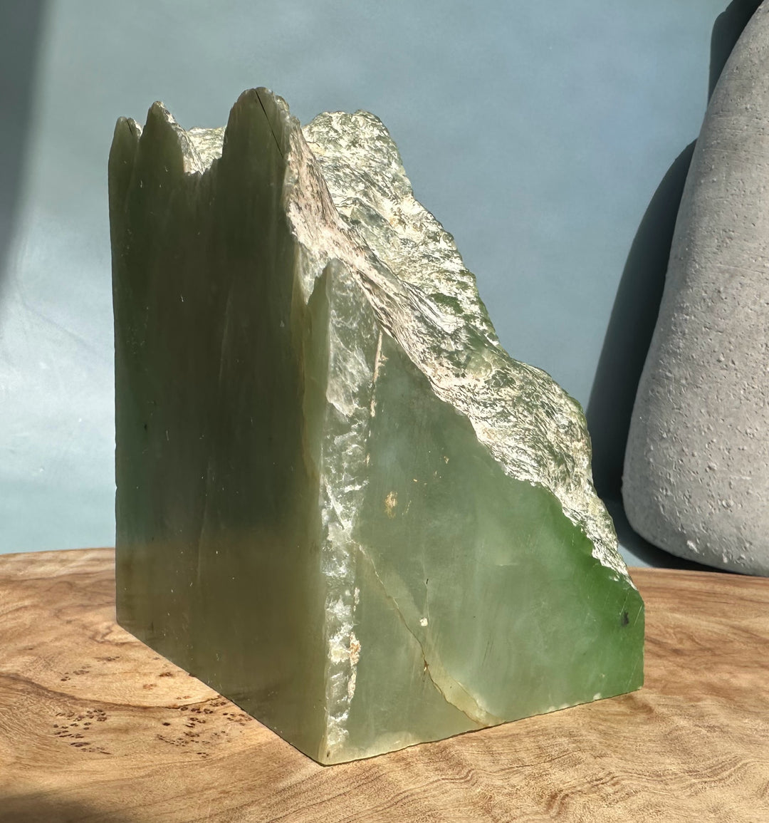 Tall nephrite jade block with jagged green crown and smooth sides on a wooden display surface