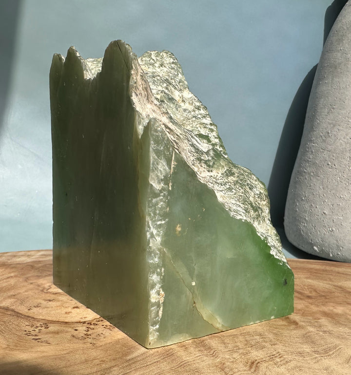 Tall nephrite jade block with jagged green crown and smooth sides on a wooden display surface