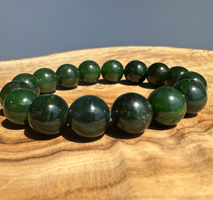 A beaded bracelet made of polished dark green gemstone-like round beads, displayed on a natural wood surface with a soft gray background.