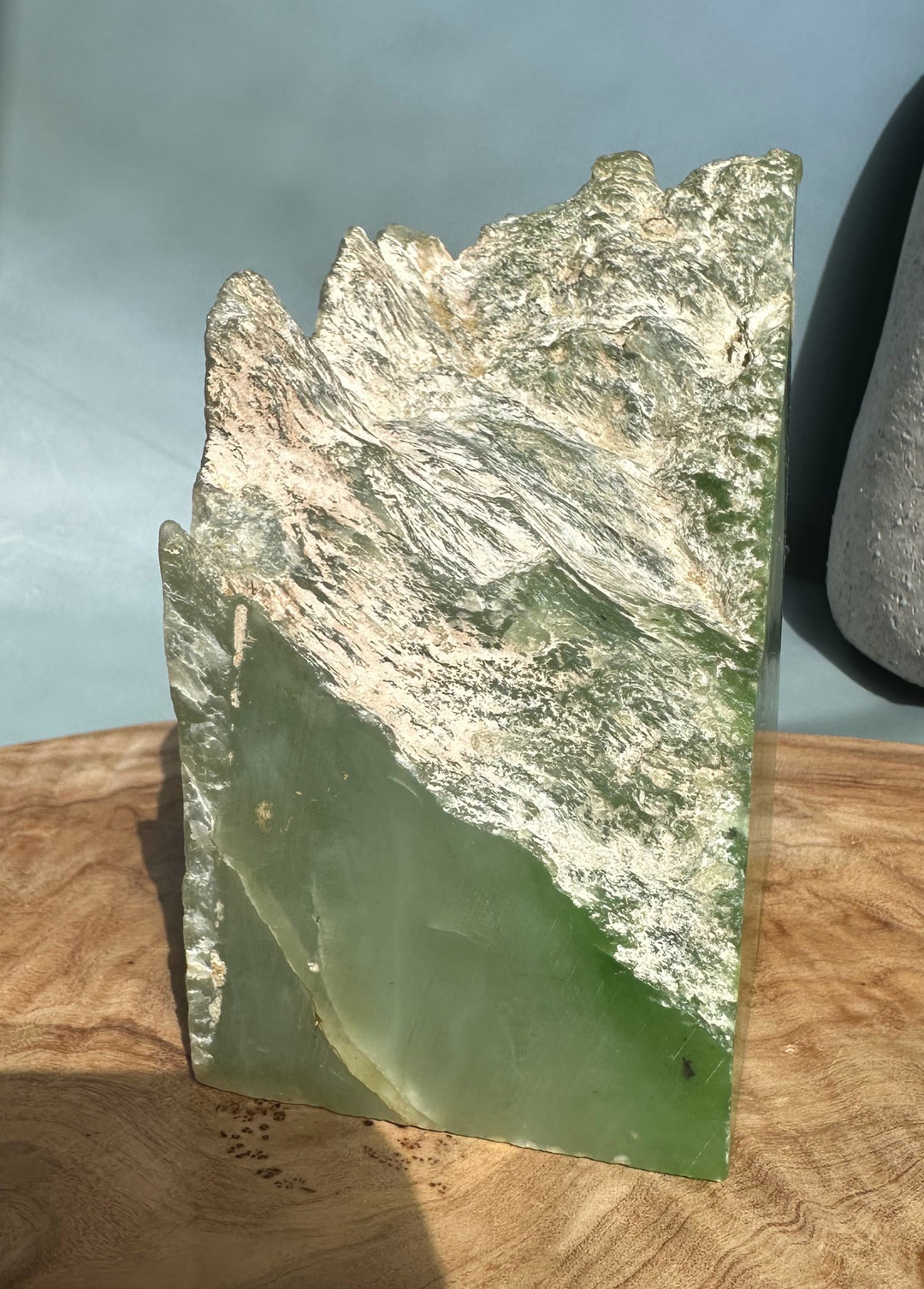 Rectangular nephrite jade slab with a rough jagged top in light green tones resting on a wooden surface