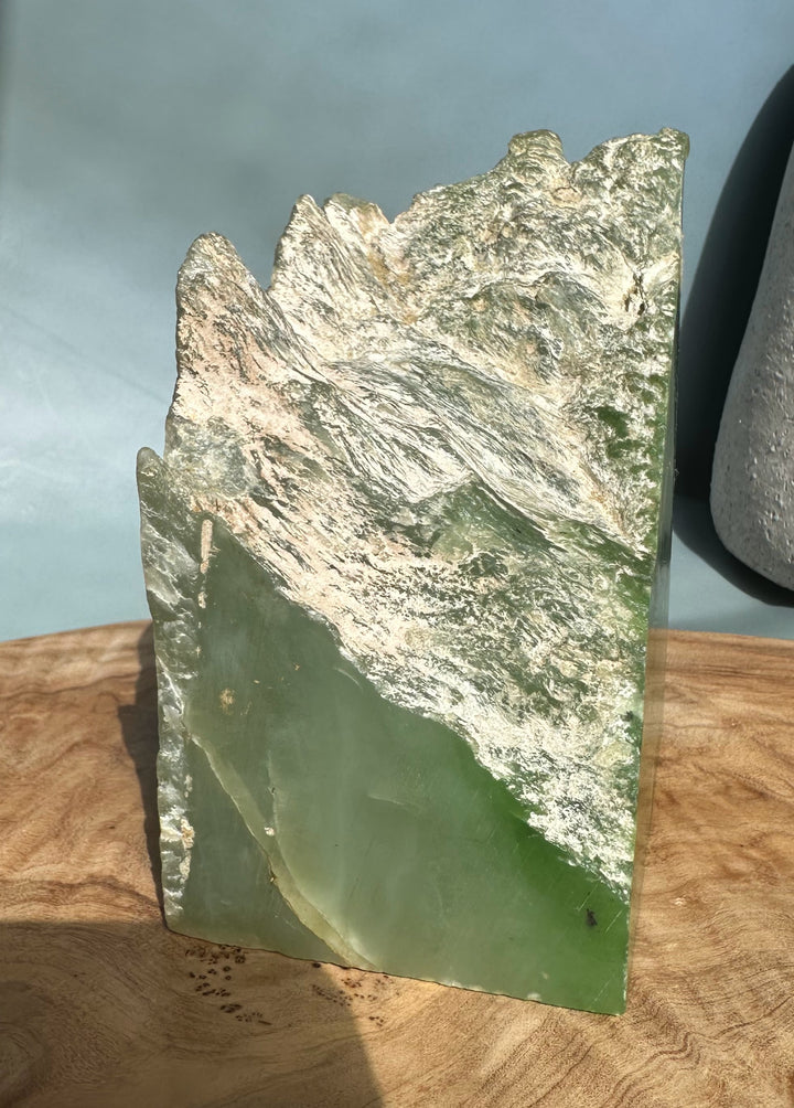 Rectangular nephrite jade slab with a rough jagged top in light green tones resting on a wooden surface