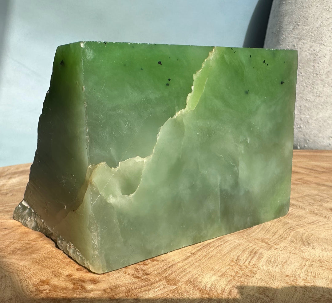 Large block of light green nephrite jade with a smooth top surface and rugged base on a wooden surface