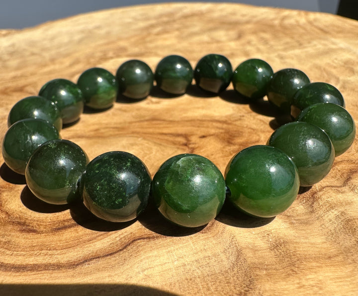 A beaded bracelet made of glossy dark green polished stone beads, arranged in a circle on a natural wooden surface.
