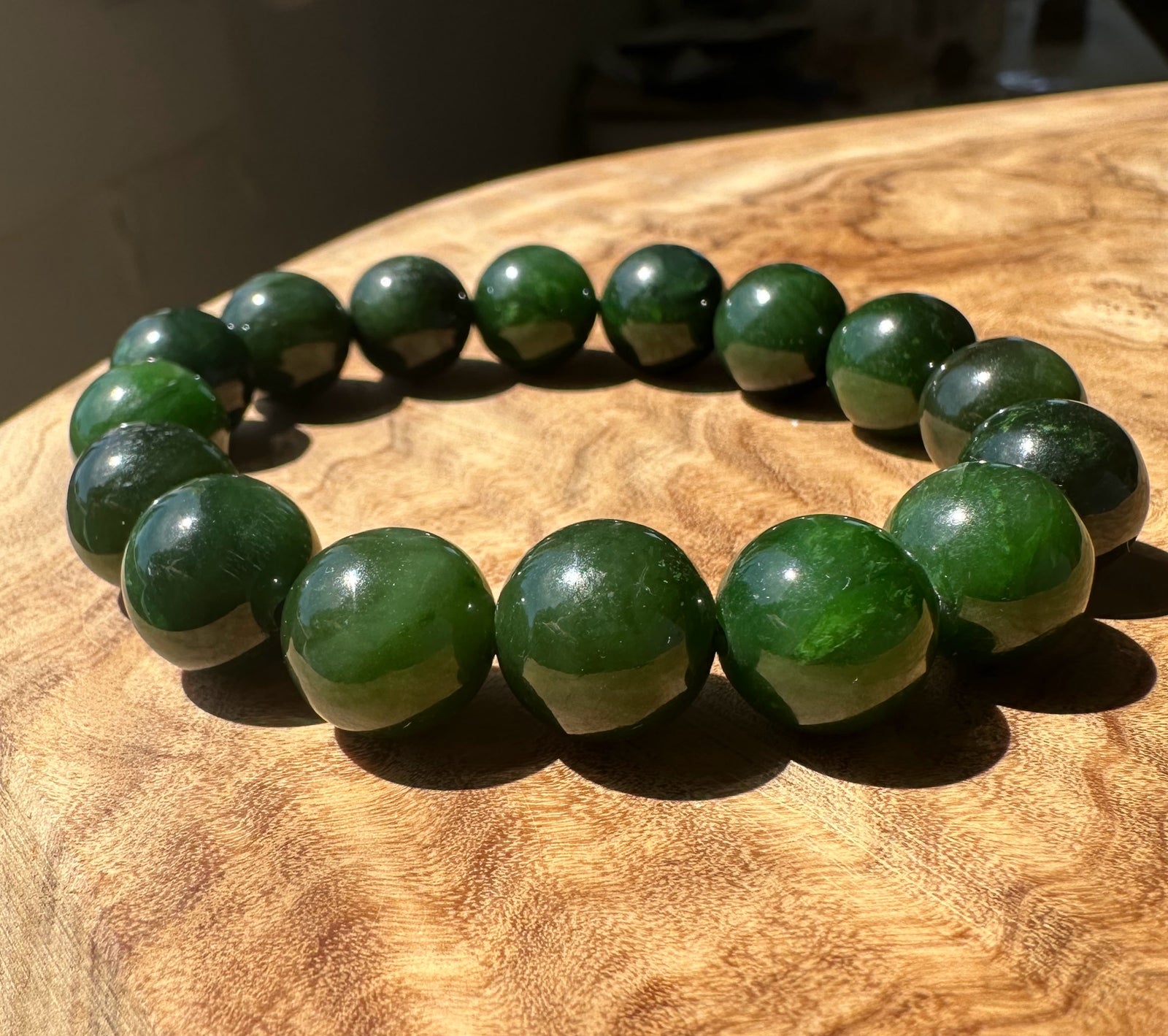 A beaded stretch bracelet made of glossy dark green round beads, displayed on a textured wooden surface.
