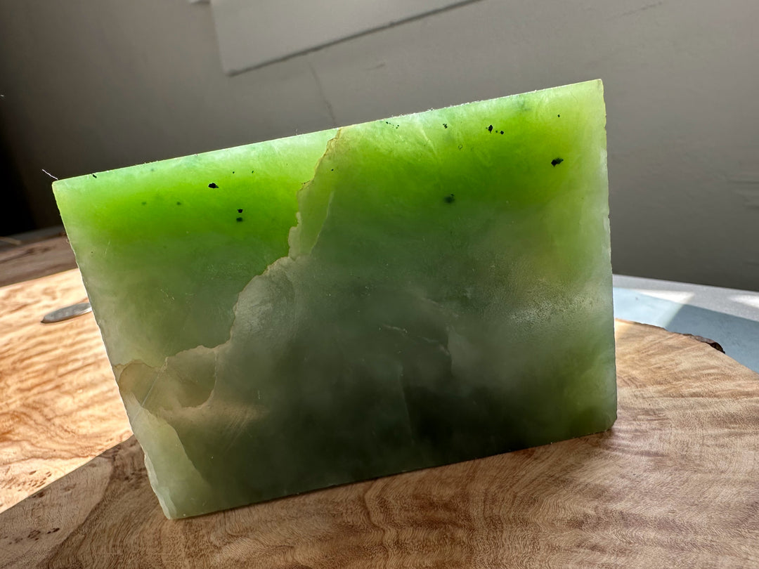 Siberian Light Green Nephrite Jade slab with bright lime green top fading to darker green at the base on a wooden surface