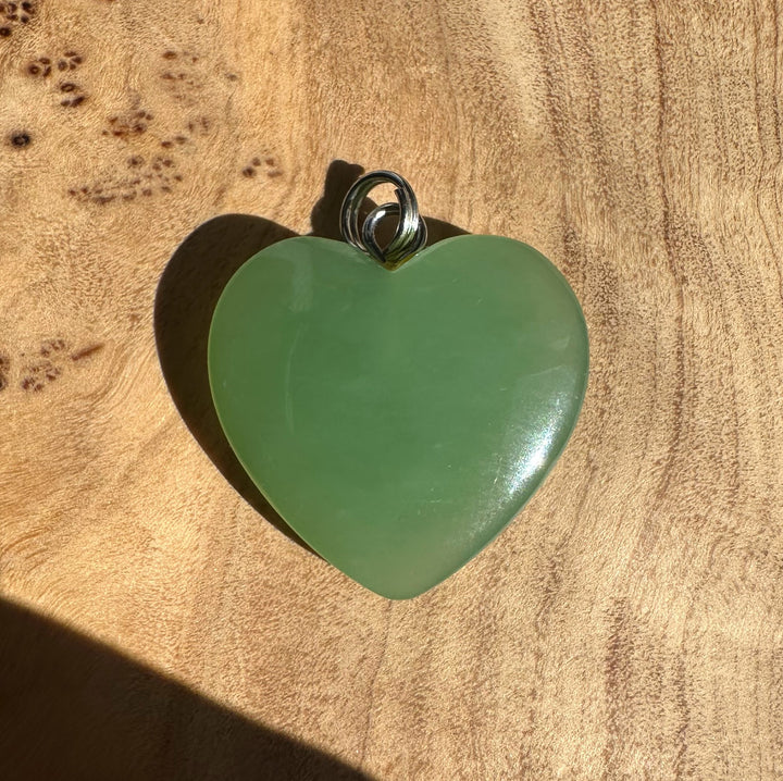 Siberian jade heart pendant 21mm with a looped silver bail on a wooden background