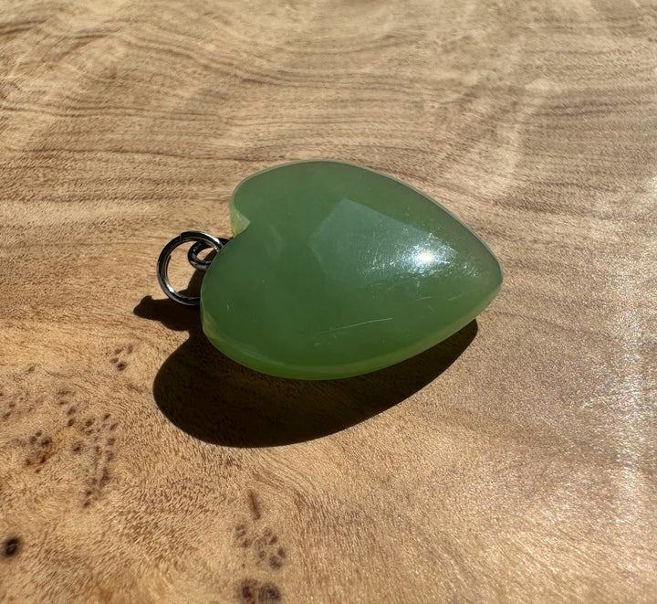 Pale green Siberian jade heart pendant with a silver loop bail on a wood surface