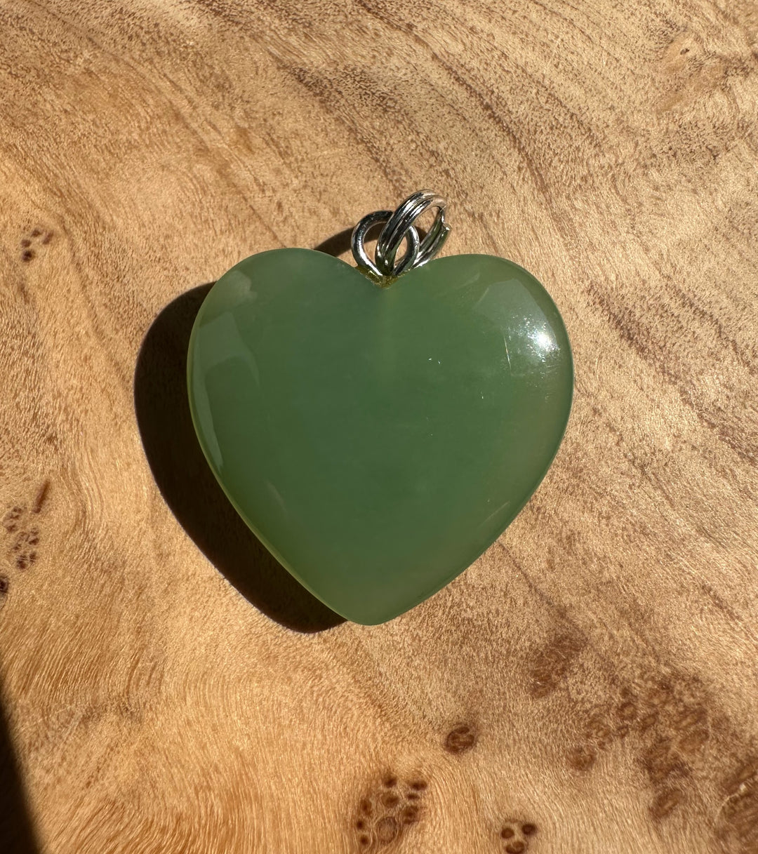 Siberian jade heart pendant with a silver bail on a wooden surface