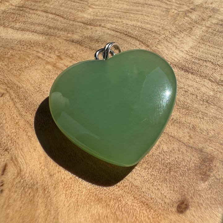 Green jade heart pendant with silver bail resting on a warm wooden background