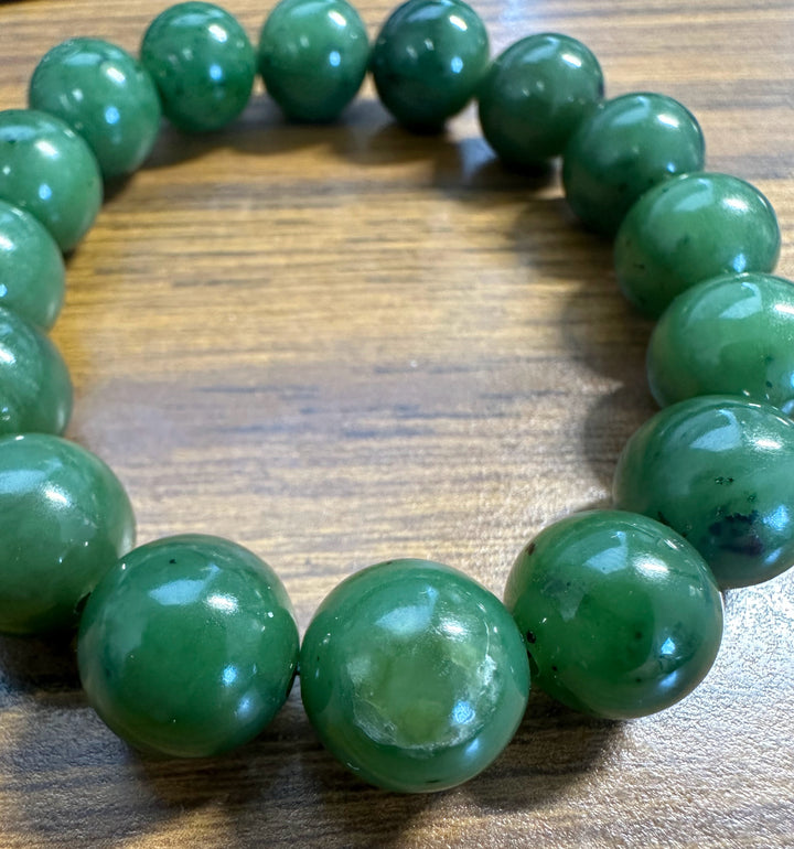 A green beaded bracelet made of glossy, polished round beads, displayed on a brown wooden surface.