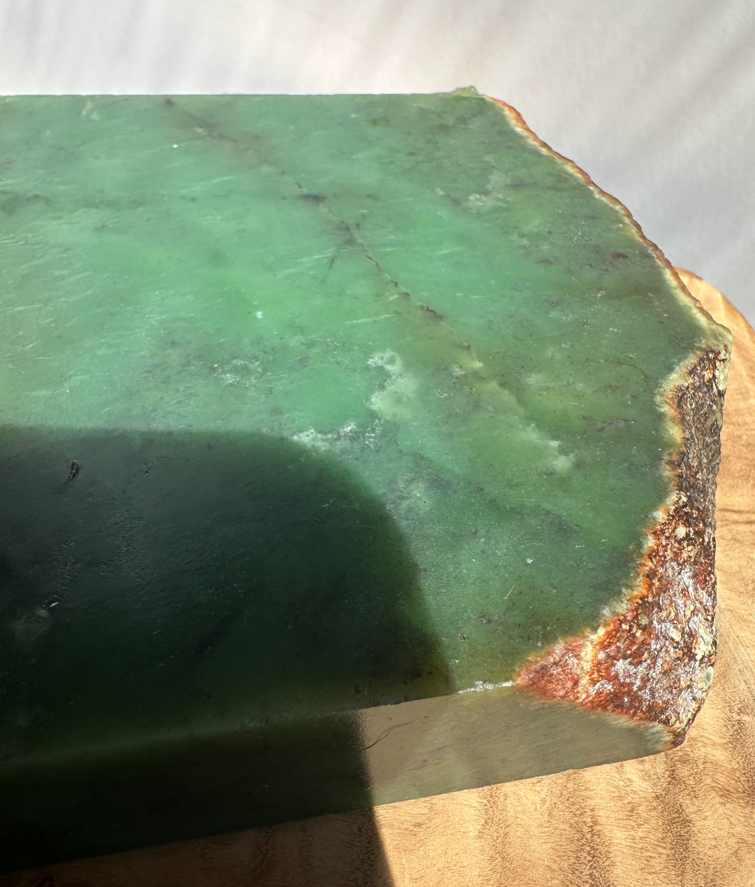 Green jade rectangular block with a rough brown and orange natural edge, photographed close up on a light surface.