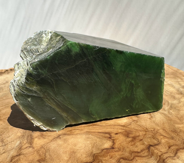 Green jade with rough natural edges, resting on a curved wooden surface against a light gray background.