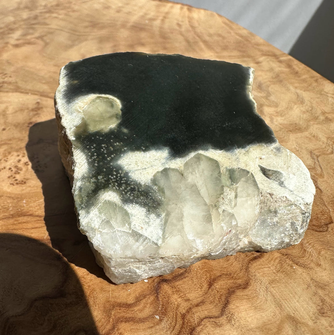 A raw jade crystal cluster specimen with a black top section and a white crystalline base, displayed on a wooden surface.