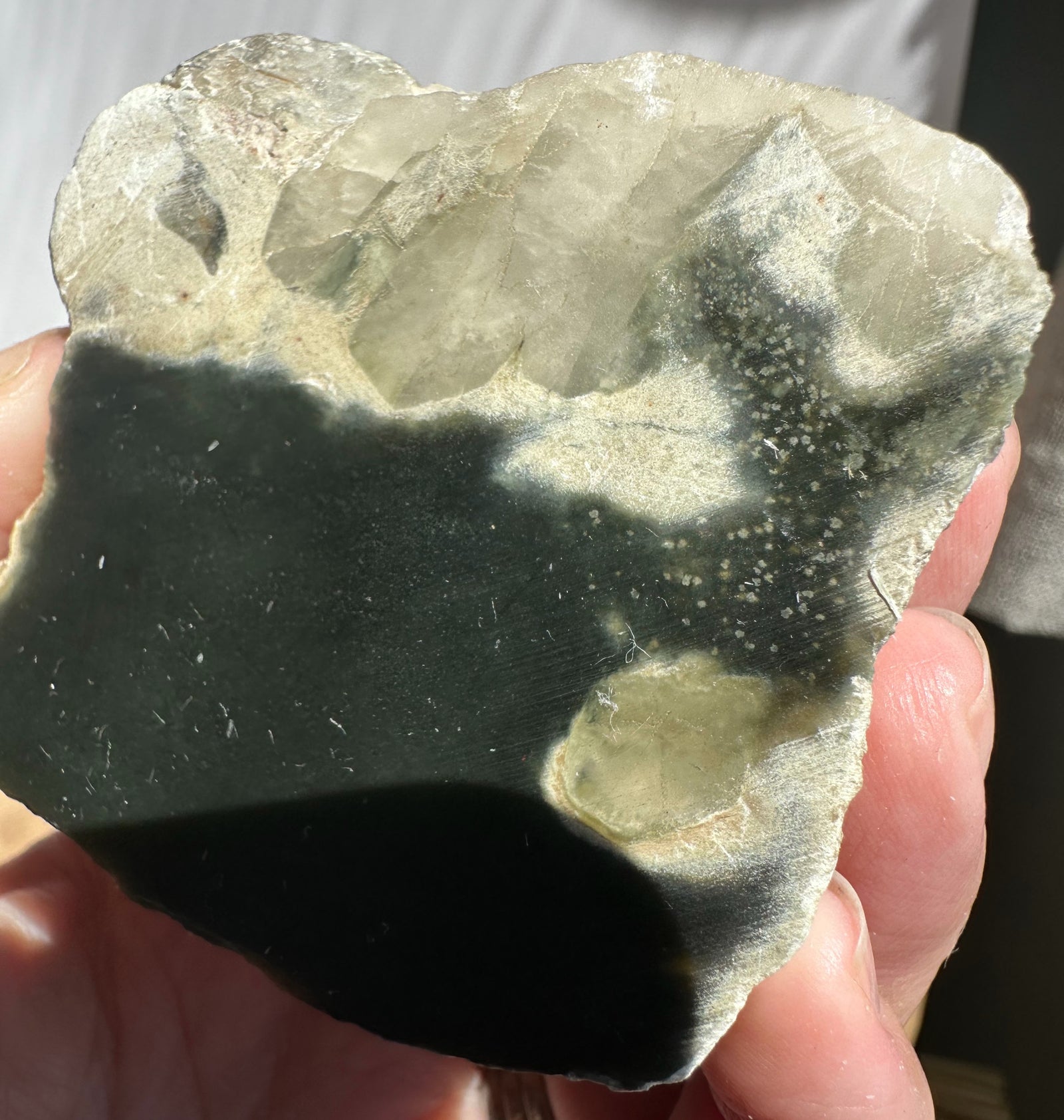 A hand holding a rough, jade  a dark green to black lower section and pale translucent crystal formations on top.