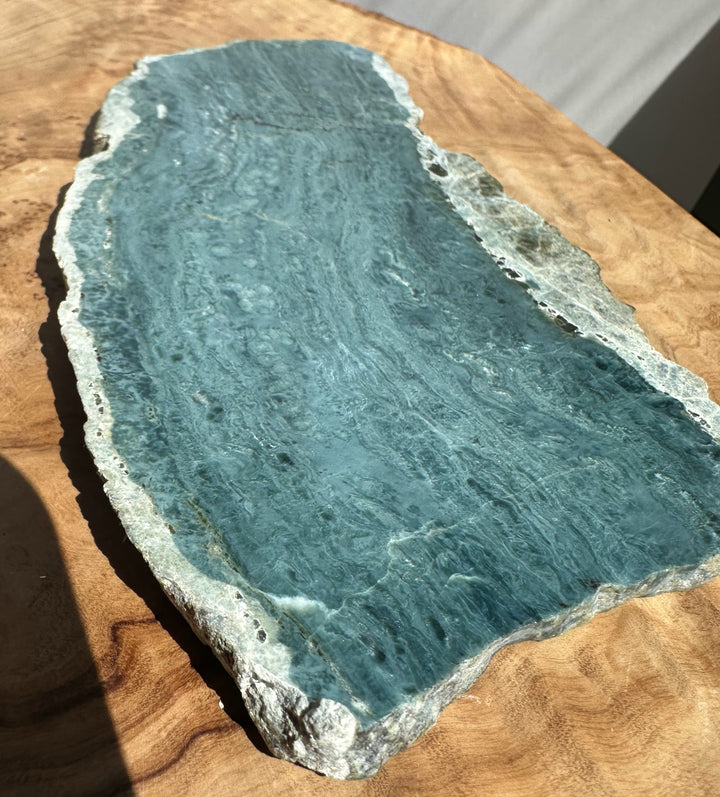 A raw stone slab with a blue-green central area and rough white-gray edges, resting on a wooden surface.