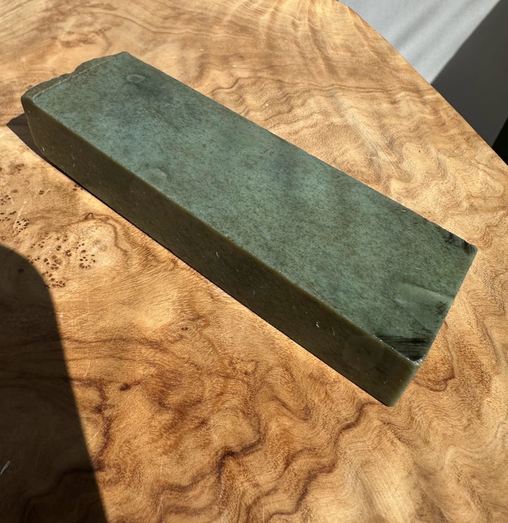 A rectangular green jade resting diagonally on a highly figured burl wood surface.