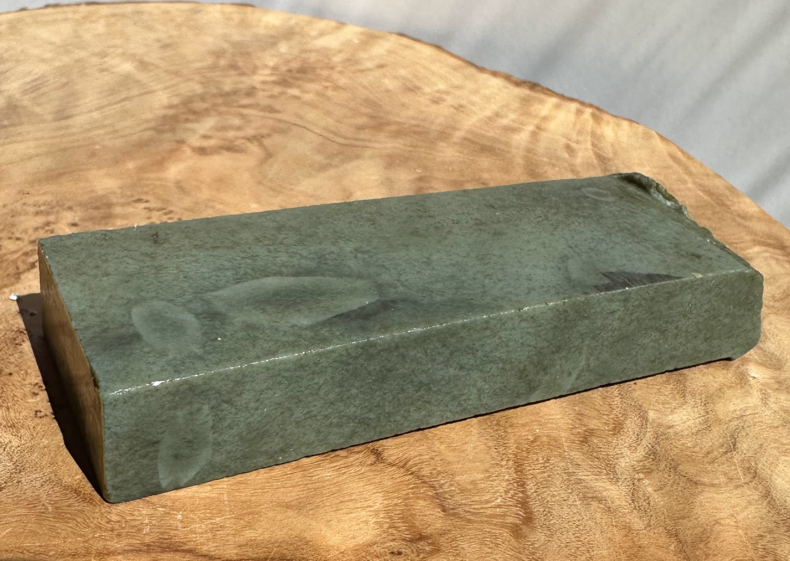 A rectangular greenjade stone resting on a round wooden slice surface.