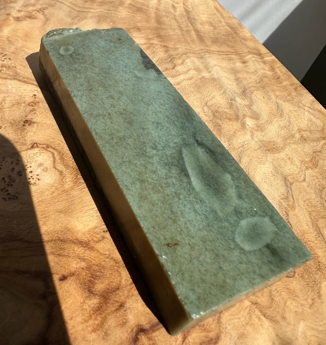 A rectangular green jade stone resting diagonally on a polished wood surface.