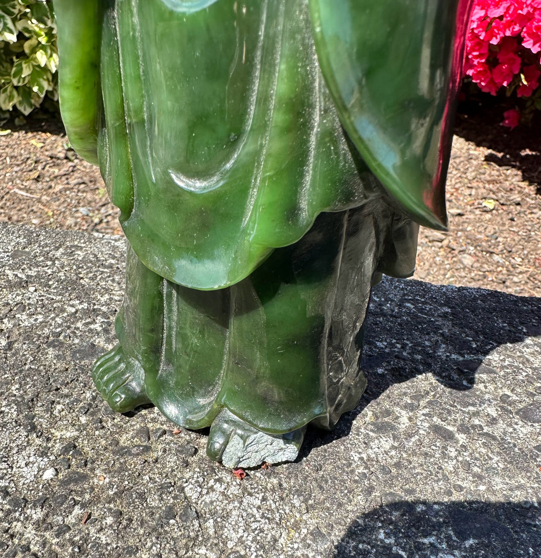 Close-up of the jade Guanyin statue base showing flowing robes and feet on a rough concrete surface